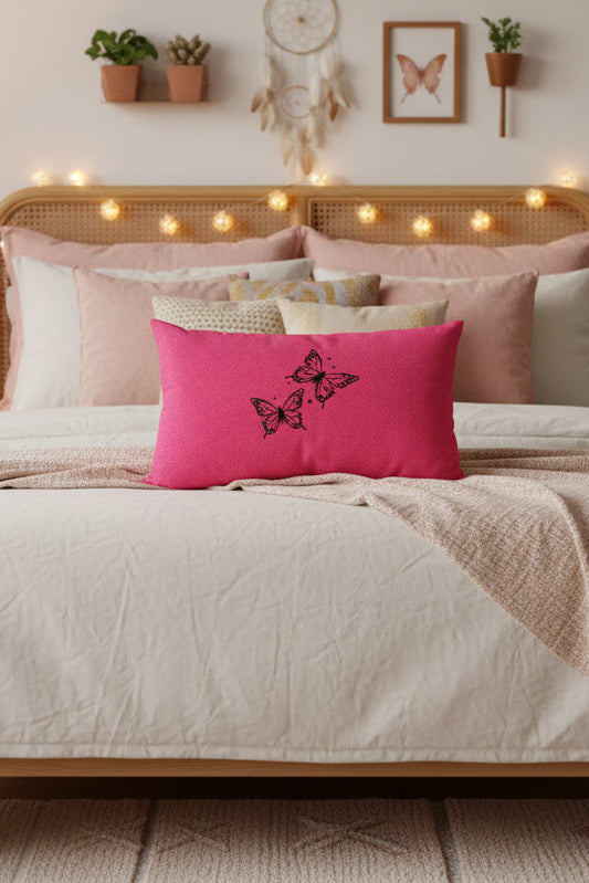 A bright pink rectangular throw pillow with two black embroidered butterflies on the front, displayed against a neutral gray background.