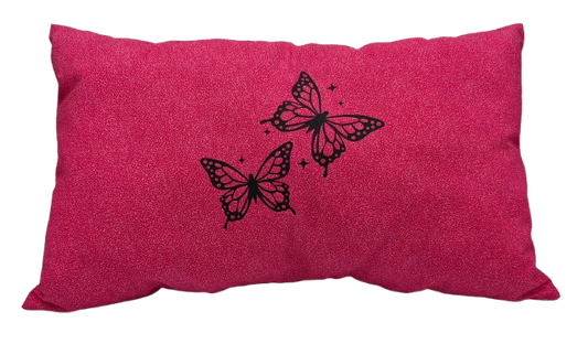 A rectangular pink throw pillow with a textured fabric surface, featuring two black vinyl butterflies and small star accents on the front.