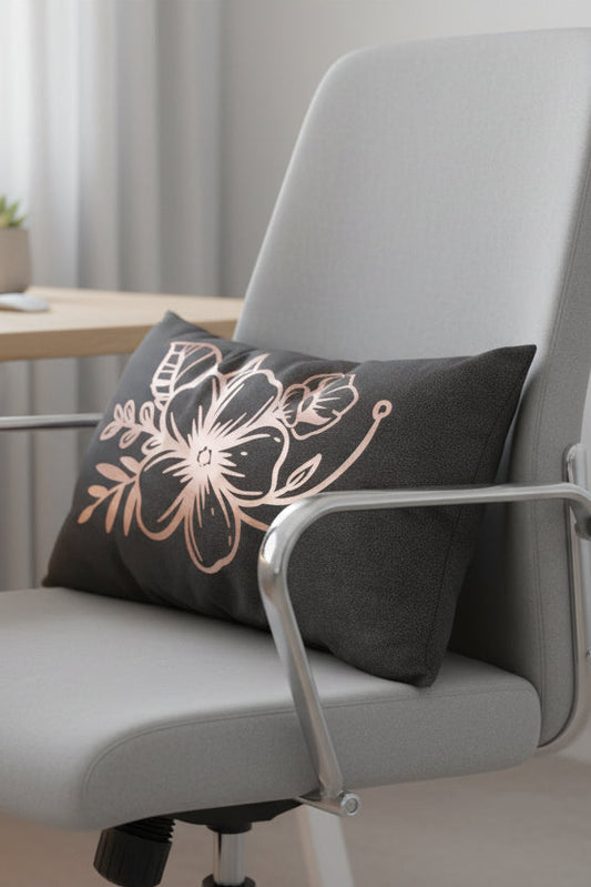 A rectangular dark gray throw pillow featuring a rose gold floral design on the front, displayed on an office chair.